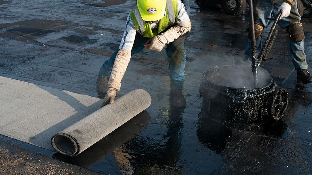 Roofer laying a membrane roll into asphalt during the GSA Bannister roof installation
