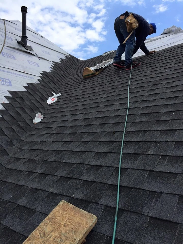 A roofer at work where exposed underlayment meets installed shingles.