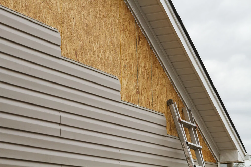 Siding being installed below the roofline, with the wall sheathing still visible.